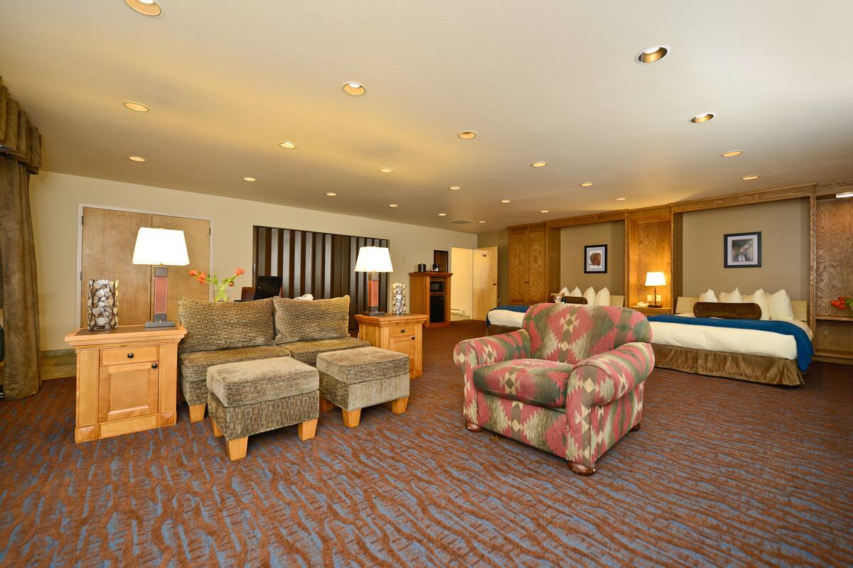 A hotel room with a sofa set, a patterned armchair, a bed, and a small table with a lamp.