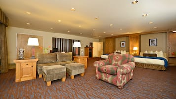 A hotel room with a sofa set, a patterned armchair, a bed, and a small table with a lamp.