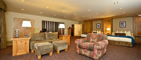 A hotel room with a sofa set, a patterned armchair, a bed, and a small table with a lamp.