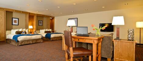 A hotel room with two beds, a desk with a laptop, a chair, a small table, and a TV.