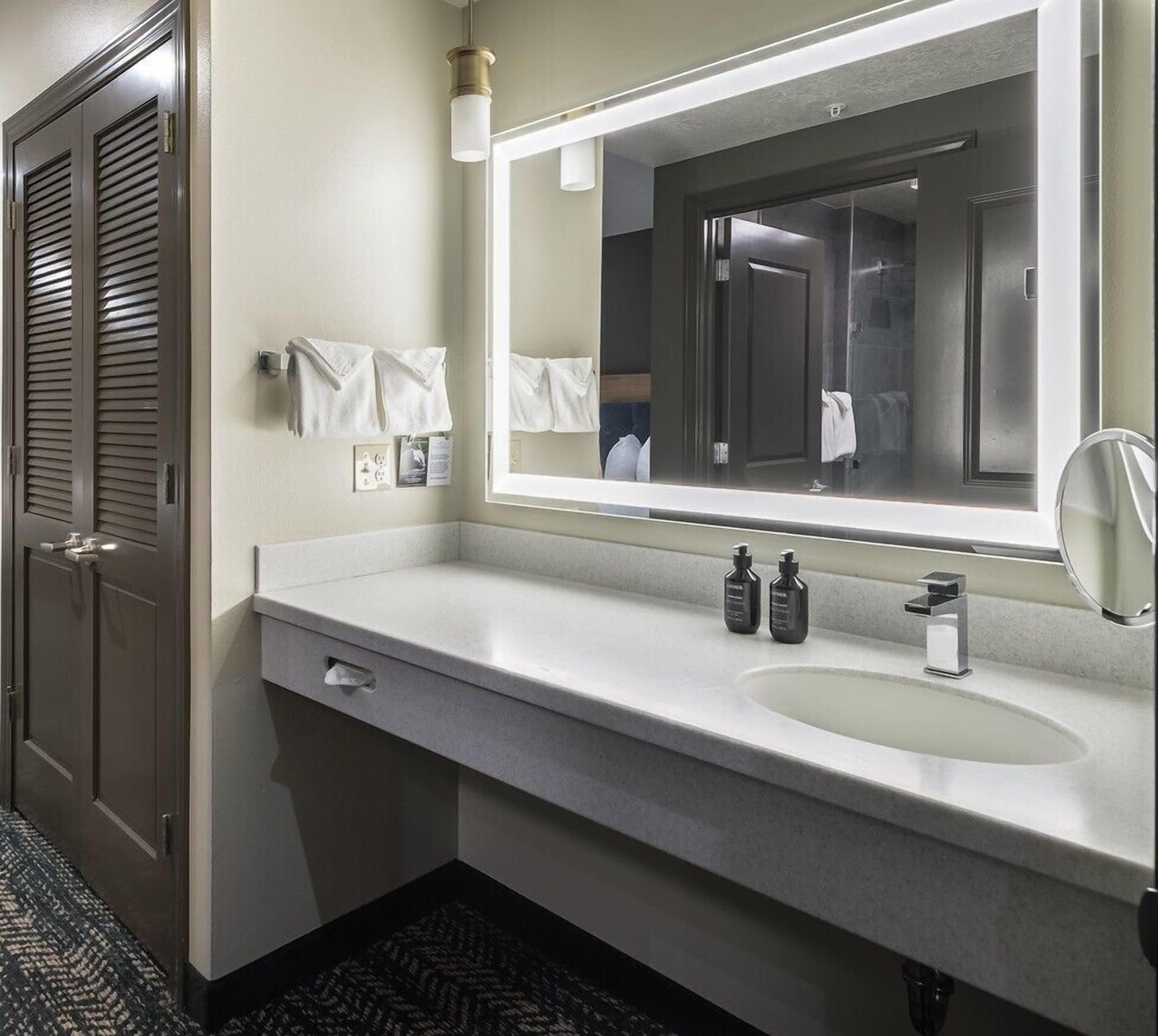 Un baño de hotel con un espejo grande, un lavamanos y un perchero para toallas.