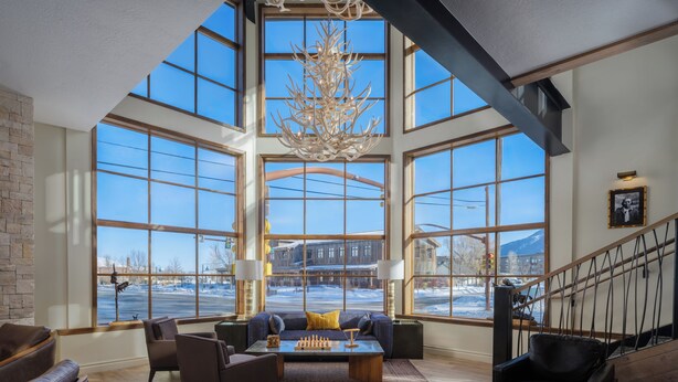 A spacious living room with large windows, a chandelier, and a view of a snowy landscape. - The Rockwell Inn (Jackson)