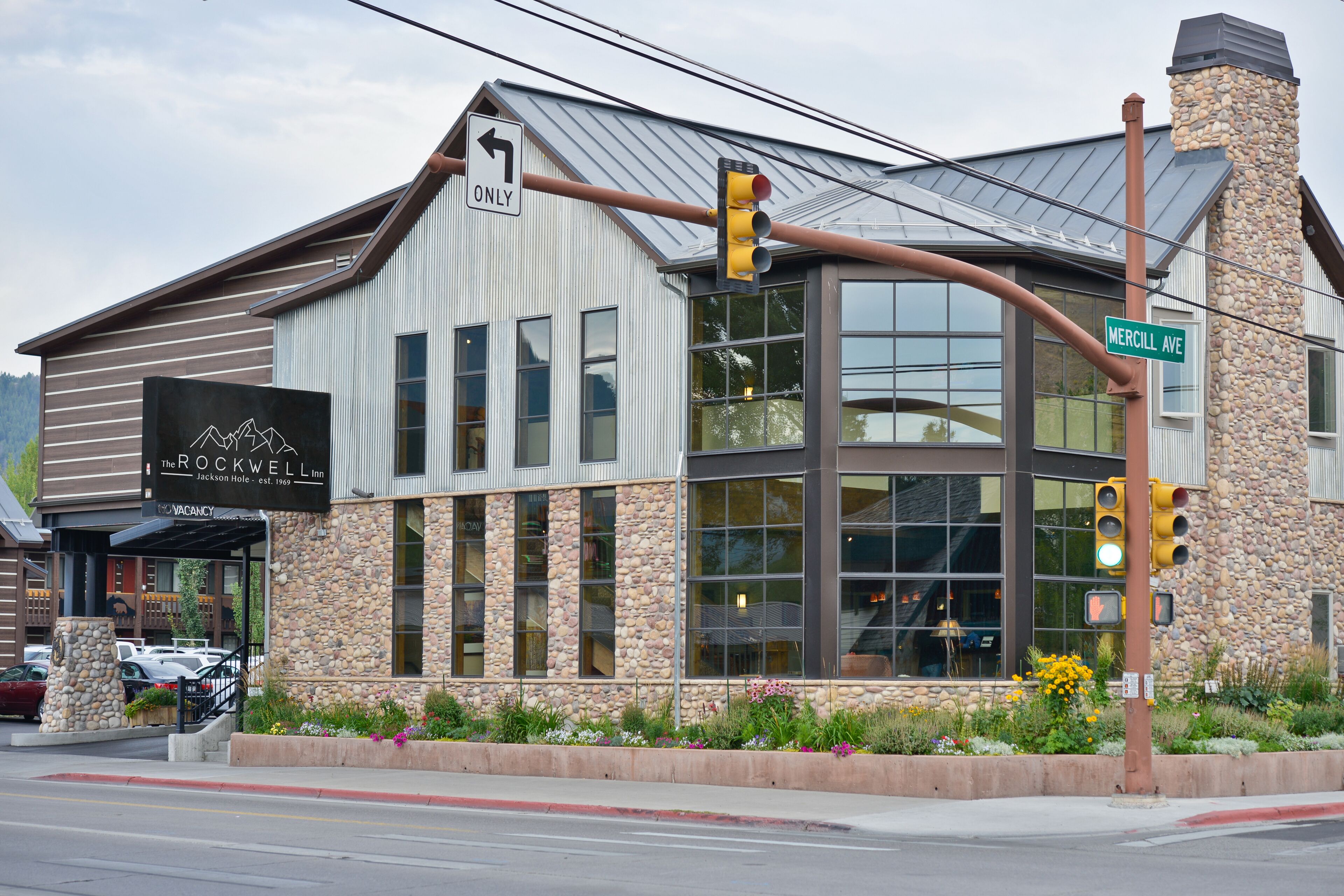 A building with a sign for 'The Rockwell' hotel, a stone facade, large windows, and a street sign for 'Mercill Ave'.