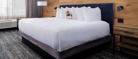 A hotel room with a large bed, a wooden headboard, a nightstand with a lamp, and a patterned carpet.