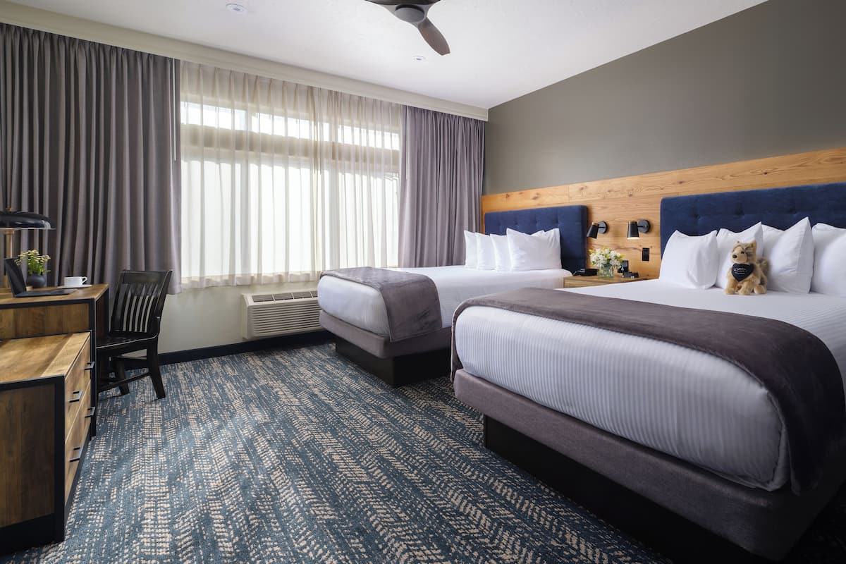 A hotel room with two beds, a desk, and a chair.
