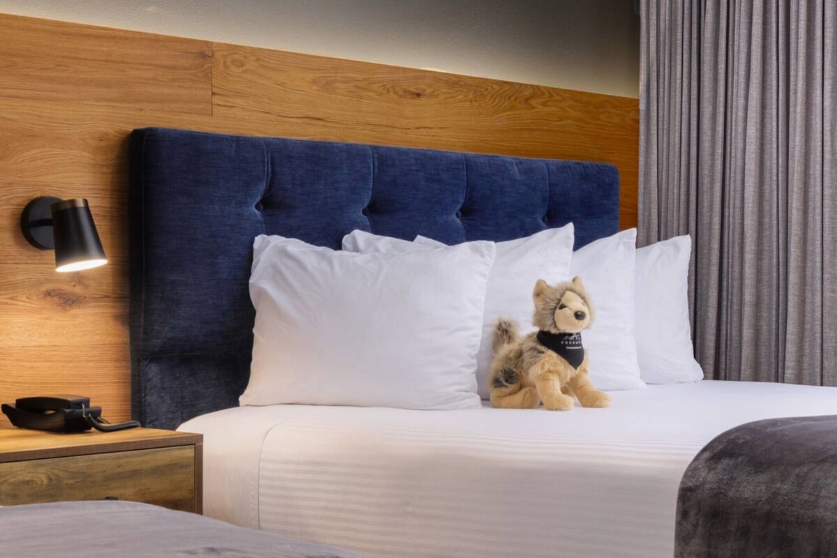 A hotel room with a wooden headboard, white bedding, and a plush toy on the bed.