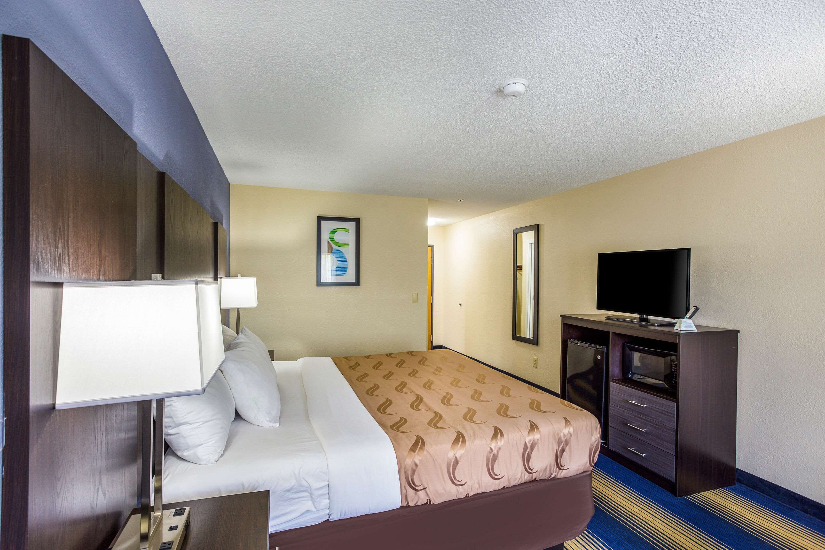 A hotel room with a bed, a desk with a lamp, a television, and a microwave.
