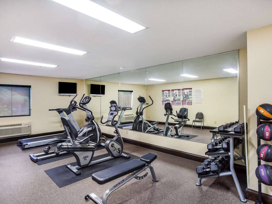 Academia com equipamentos de ginástica, espelho e suporte para halteres na parede.