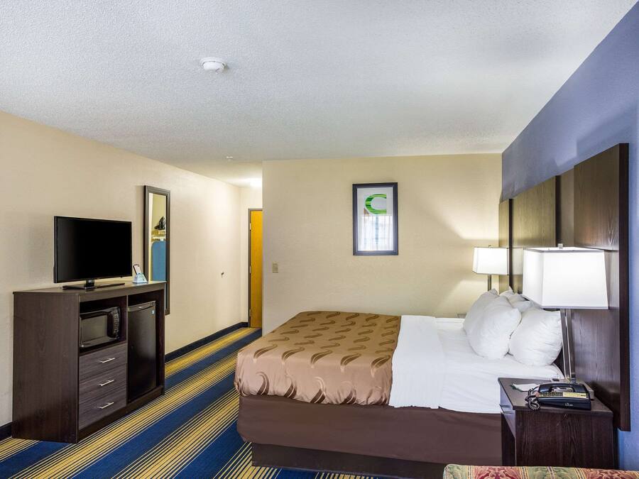A hotel room with a bed, a TV, a desk with a microwave, and a lamp.