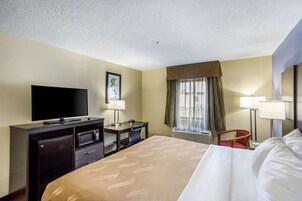 Habitación de hotel con cama, escritorio con computadora, televisor, microondas y ventana con cortinas.