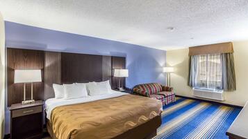 A hotel room with a large bed, a nightstand, a chair, and a window with curtains.