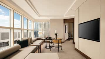Una habitación de hotel moderna con un ventanal grande, un sofá, una mesita, una silla y un televisor de pantalla plana.