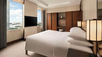 A hotel room with a large bed, a TV mounted on the wall, a nightstand, and a view of a cityscape through a large window.