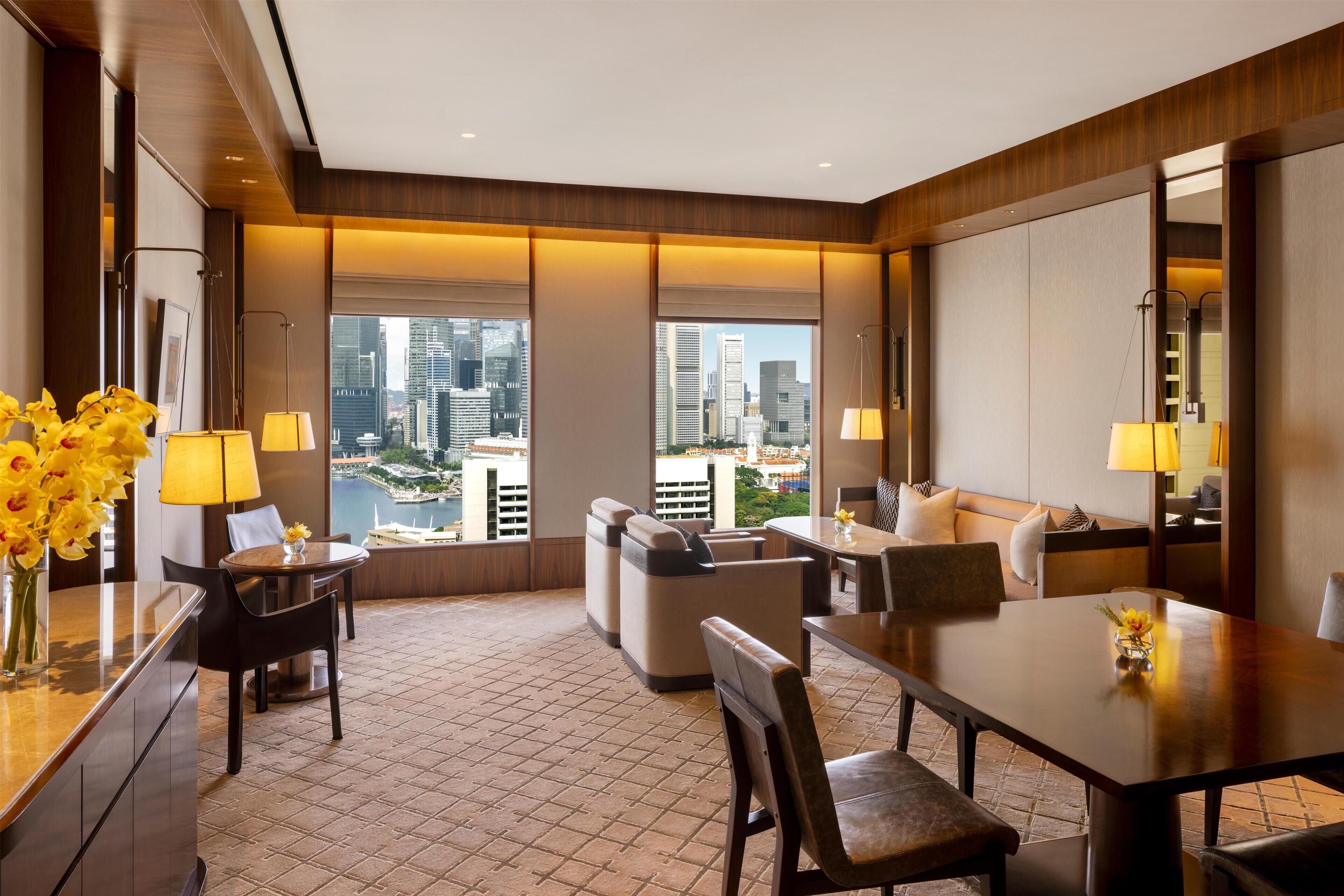 Habitación de hotel moderna con vistas a la ciudad, zona de comedor y sala de estar con sofá y sillones.