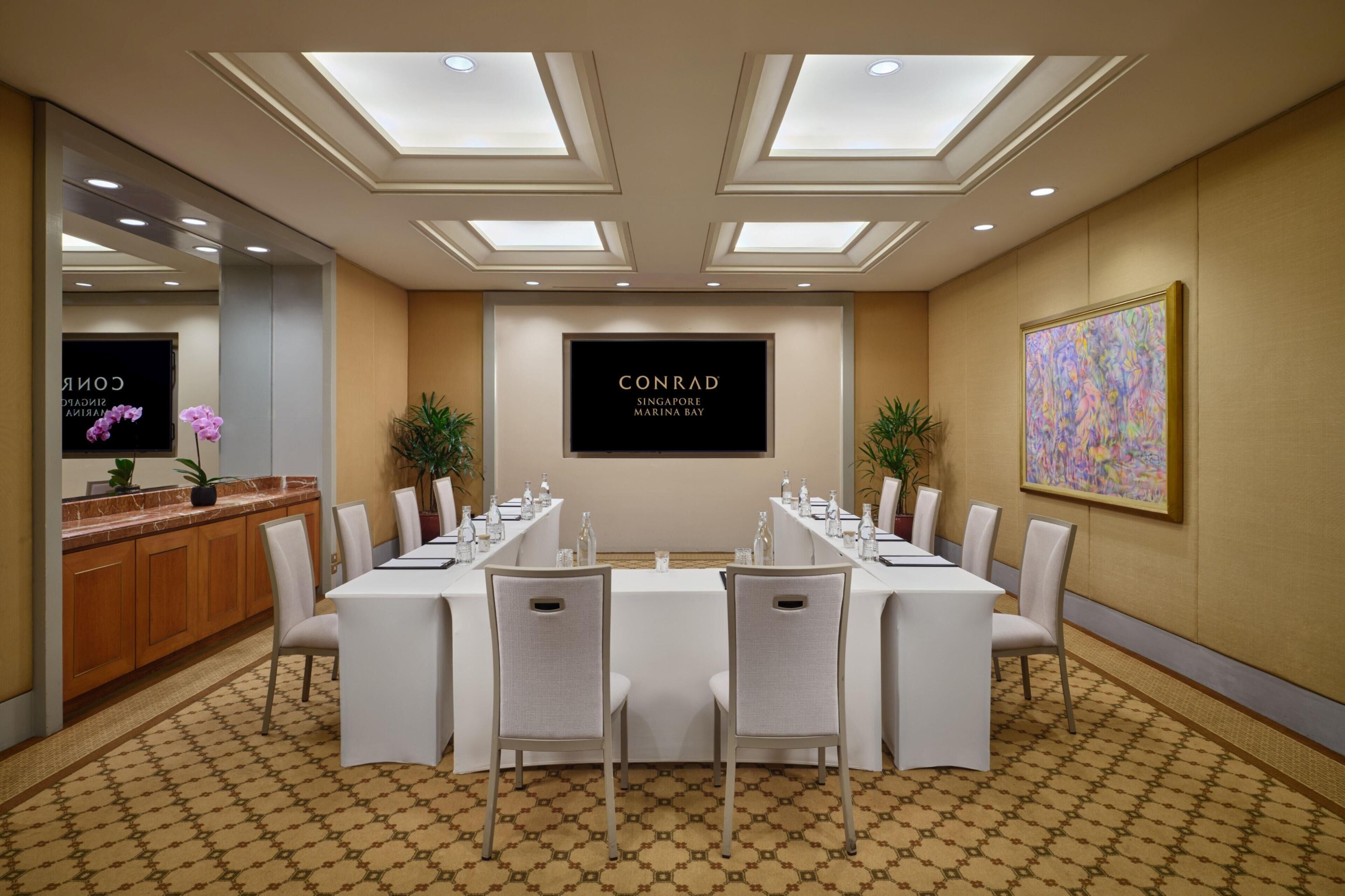 A conference room with a long table, chairs, a reception desk, and a framed sign on the wall.