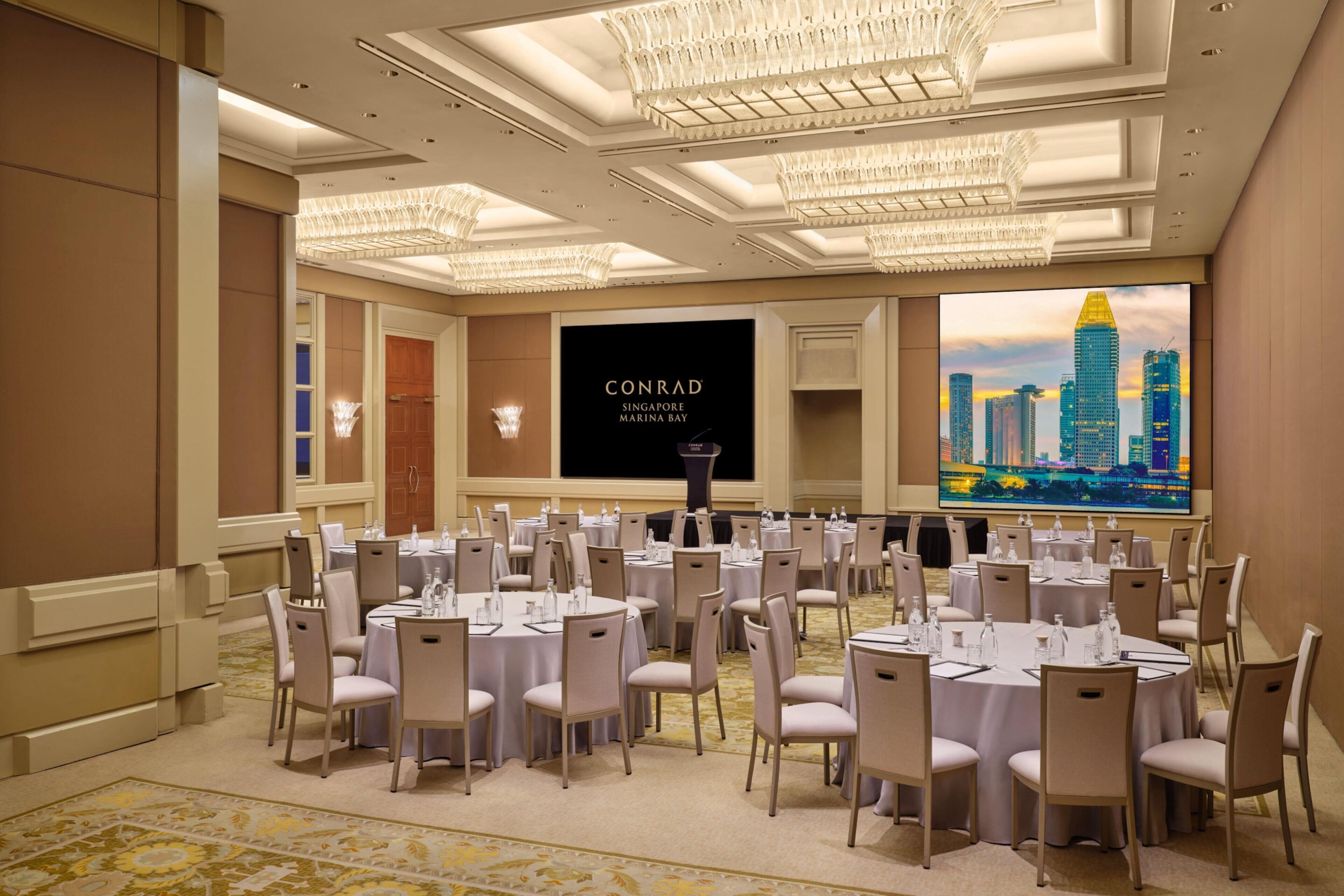 A conference room with round tables, chairs, and a large screen displaying a cityscape.