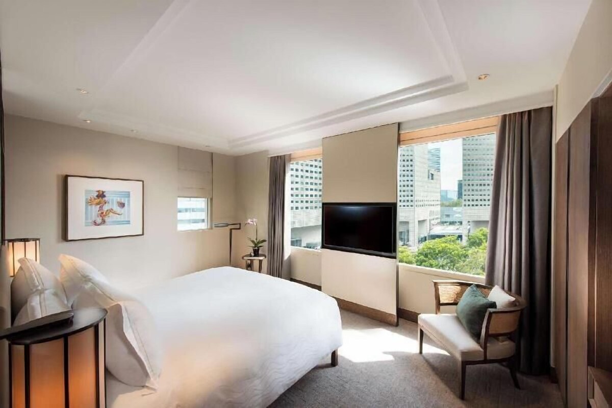 Une chambre d’hôtel équipée d’un lit, d’une télévision, d’un bureau, d’une chaise et d’une fenêtre donnant sur la ville.