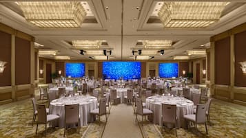 Salão de banquetes com mesas redondas, lustres e um fundo com efeito de céu estrelado.