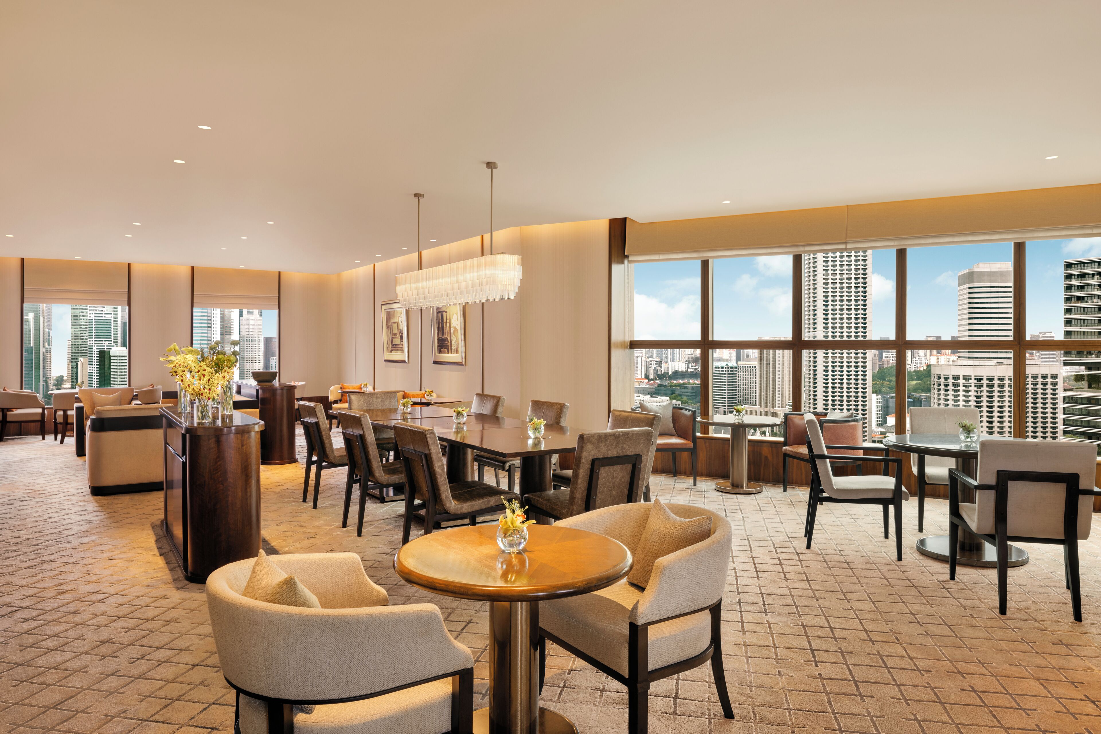 Un amplio vestíbulo de hotel con varias zonas de estar, grandes ventanales con vistas a la ciudad y una decoración moderna.