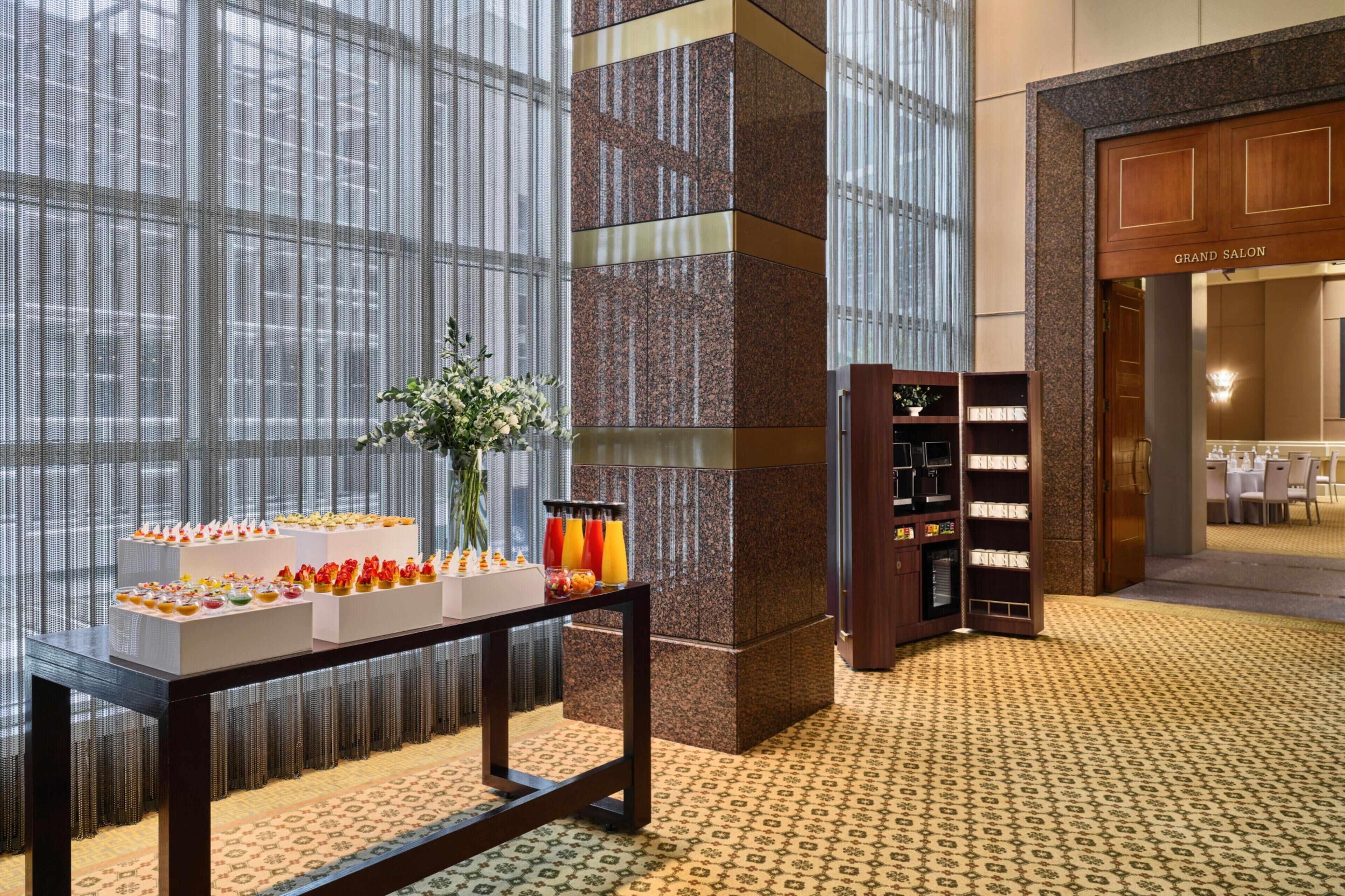 A hotel lobby with a display table, a bookshelf, and a view of the Grand Salon.