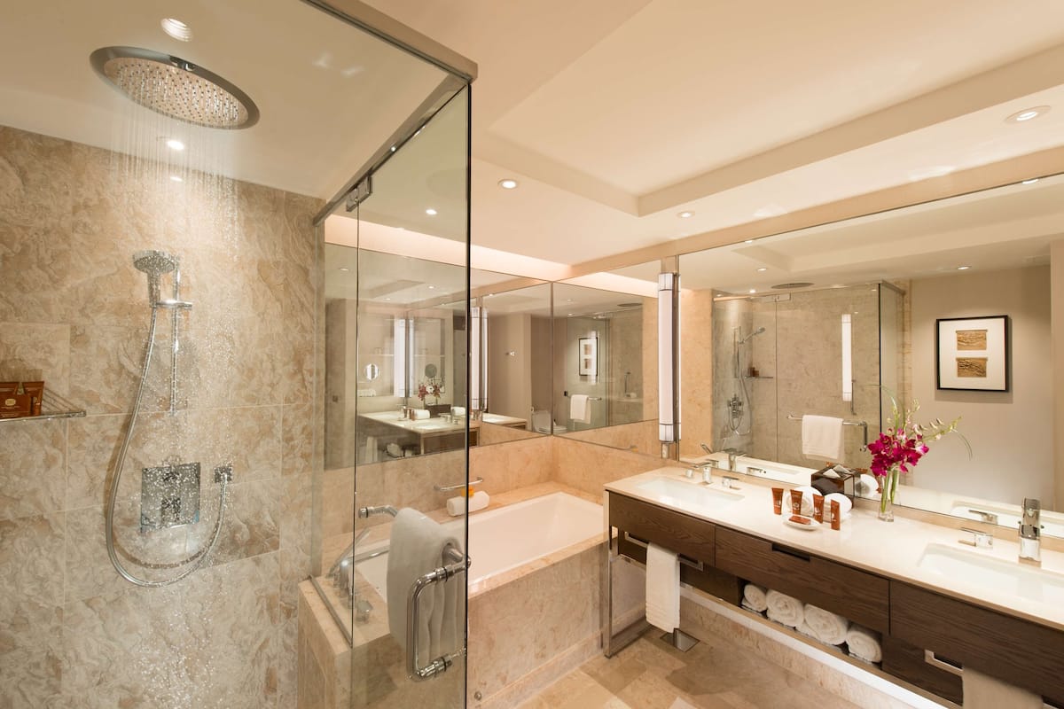 Un baño moderno con ducha de vidrio, un espejo grande, una bañera y un tocador con artículos de aseo.