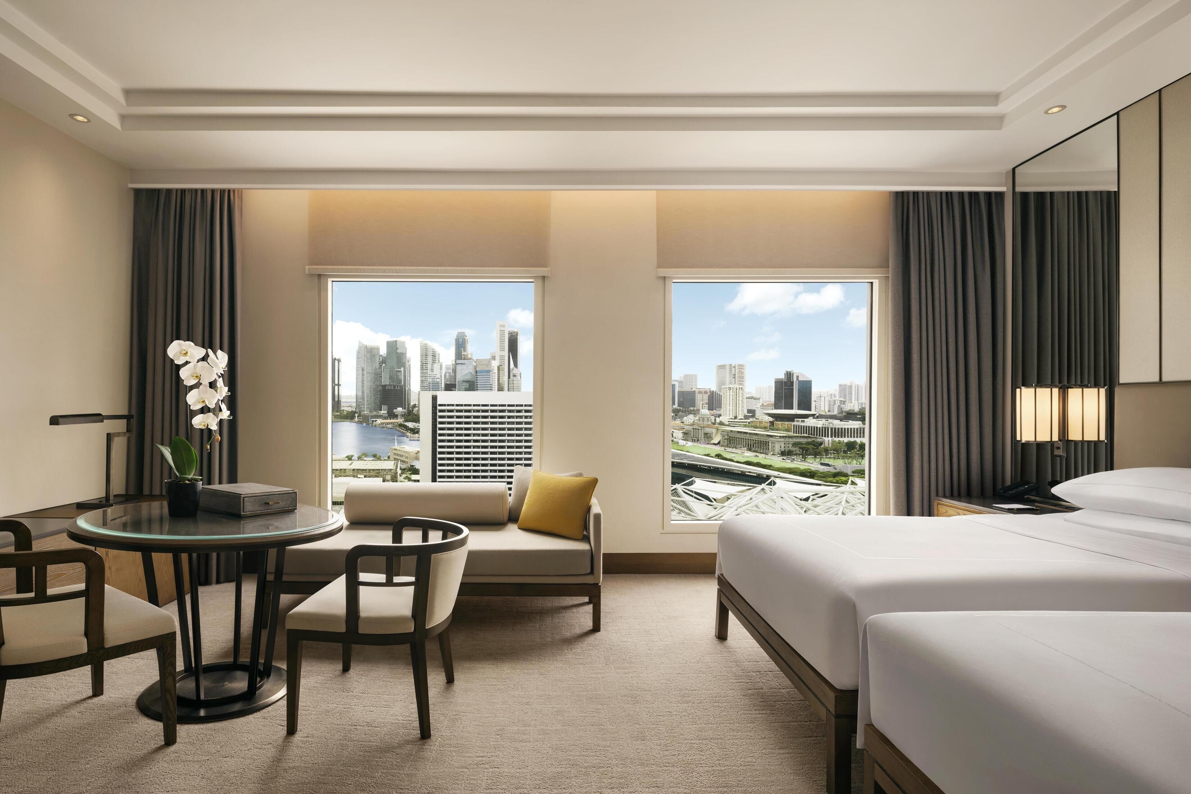 A hotel room with a city view, a round glass table, a sofa, and a bed.