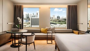 Une chambre d’hôtel avec une grande fenêtre, un canapé, un lit, une petite table et une chaise.