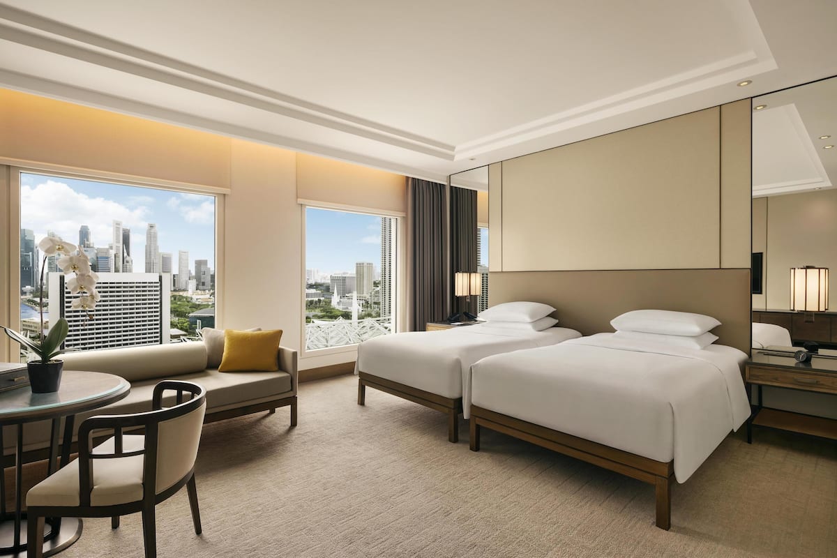 Habitación de hotel con dos camas, un sofá, un escritorio y vistas a la silueta urbana.