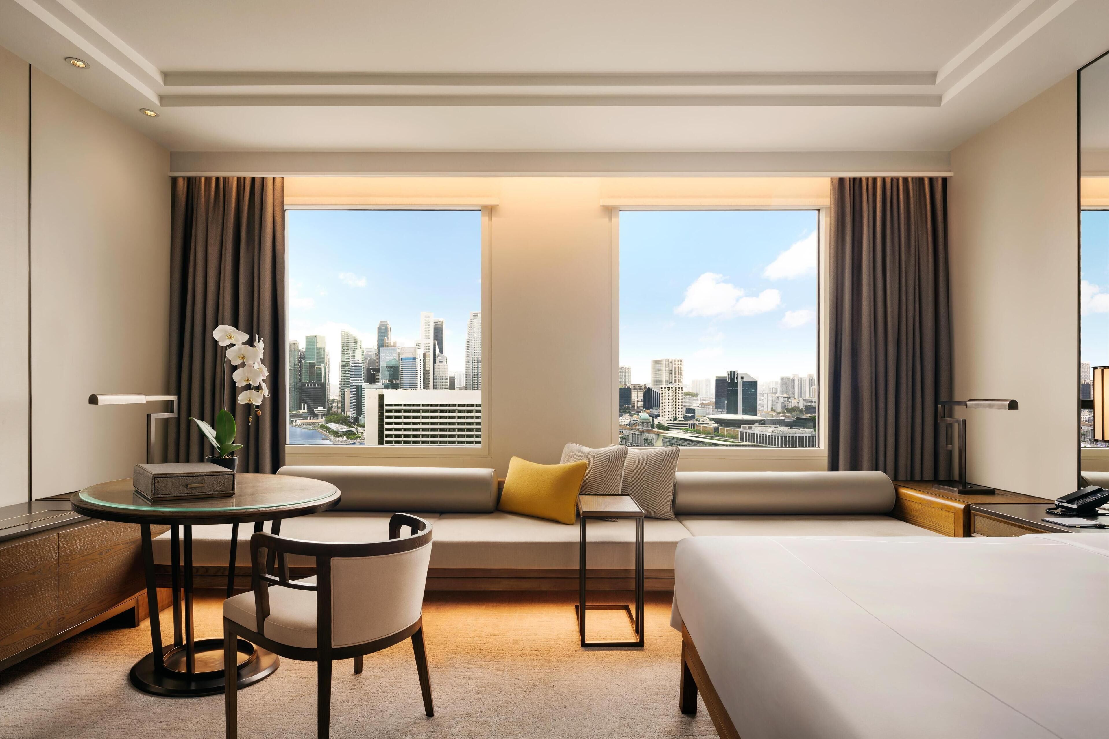 Une chambre d’hôtel avec une grande fenêtre, un canapé, une petite table, une chaise et un lit.