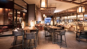 Un hall d’hôtel moderne doté d’un bar, de coins salon et offrant une vue sur la cuisine.