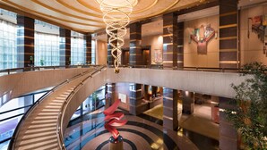 Un hall d’hôtel moderne, doté d’un lustre central en forme de spirale, d’un escalier en verre et d’un comptoir d’accueil.
