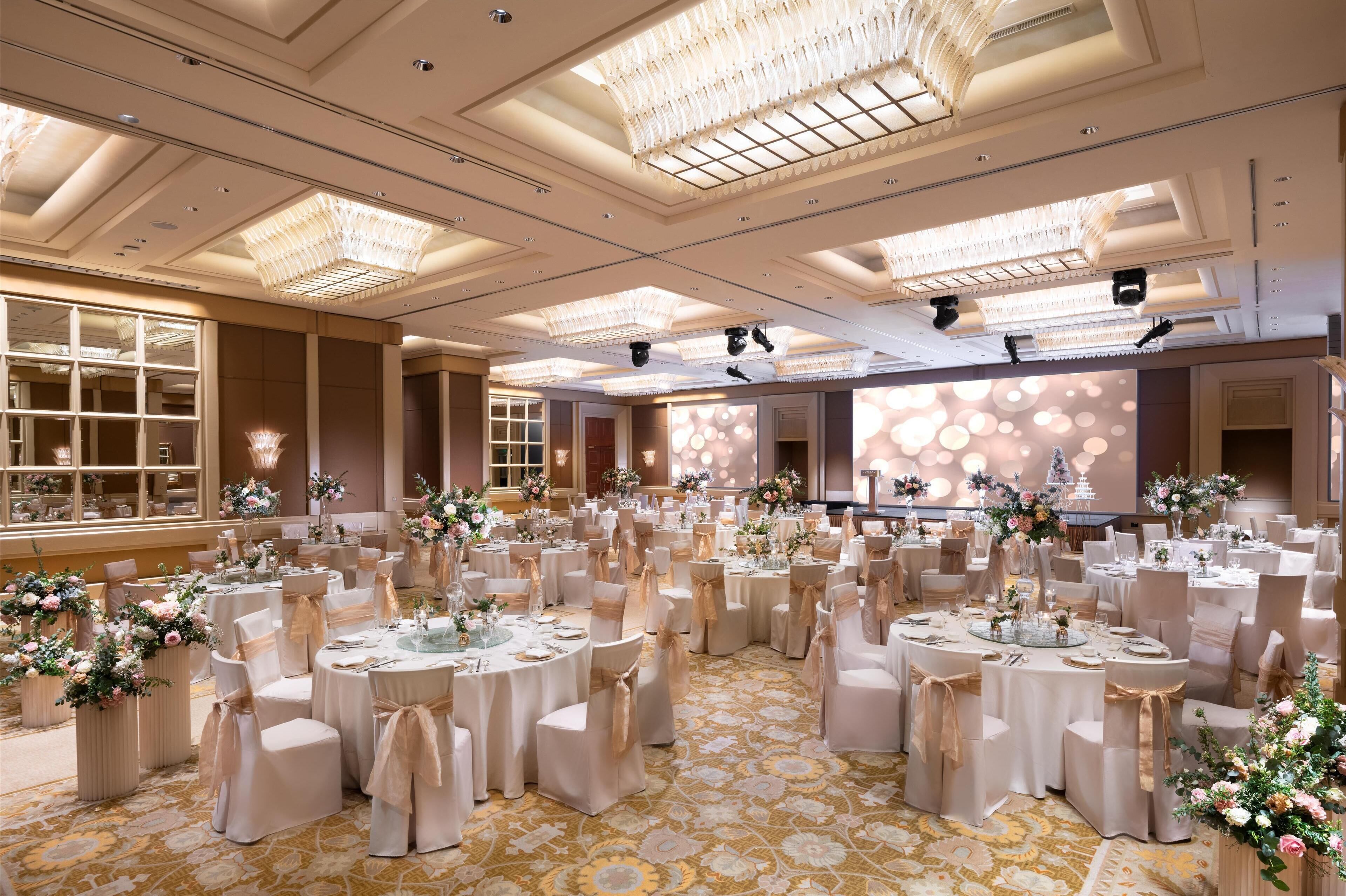 A banquet hall with round tables, white tablecloths, and floral centerpieces.