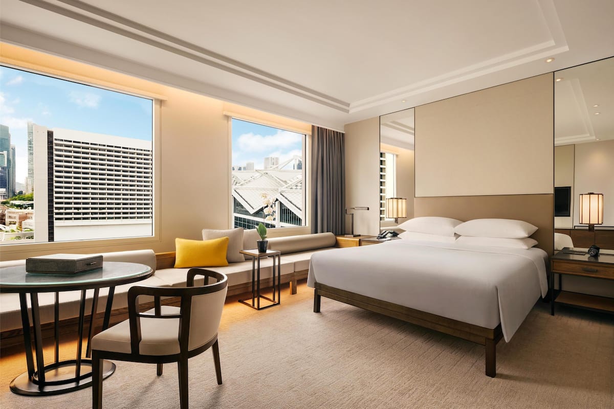 Una habitación de hotel moderna con una cama grande, un área de descanso con una mesa y vistas a la ciudad.