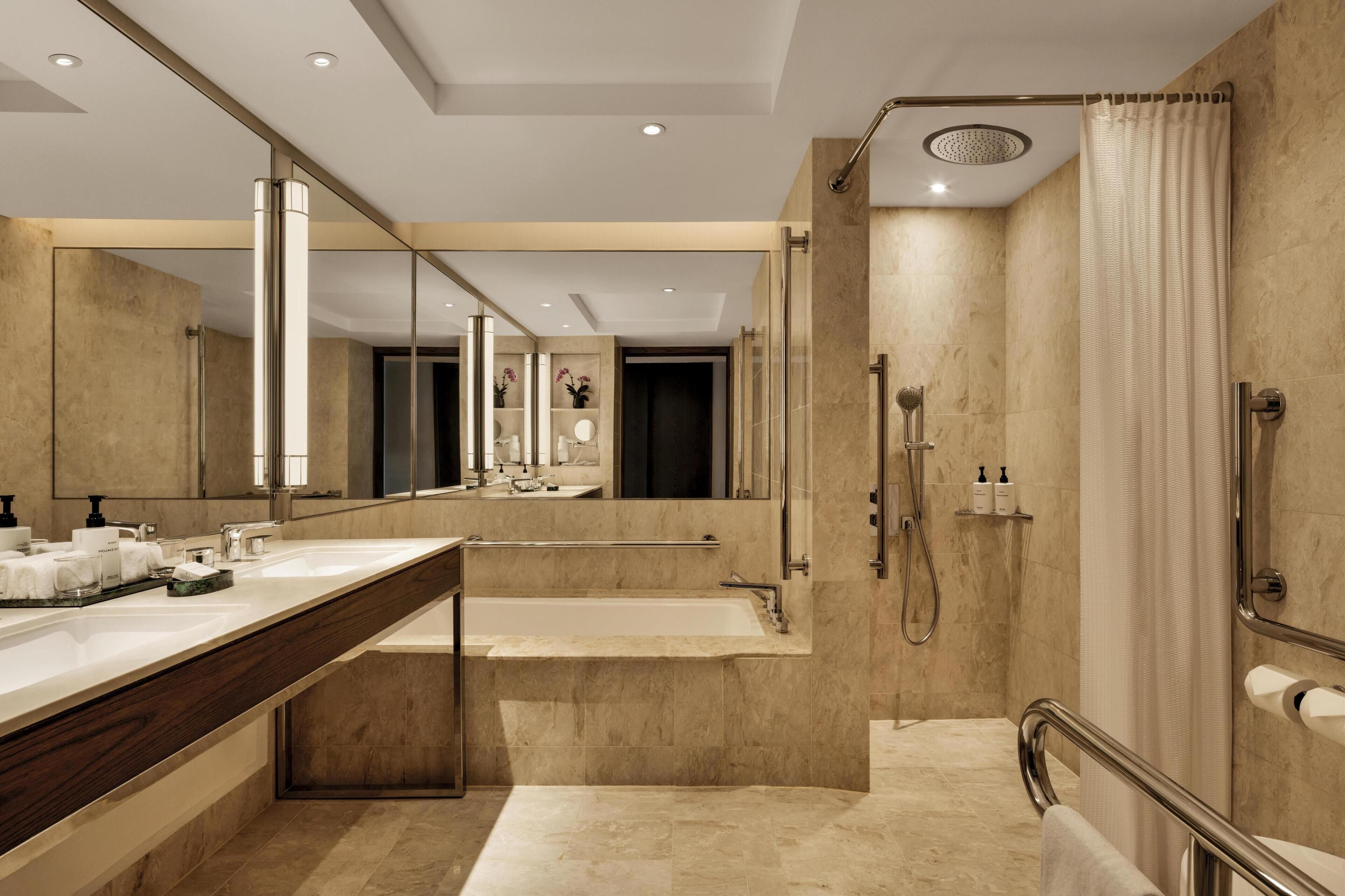 A modern bathroom with a large mirror, dual sinks, a bathtub, and a shower area.