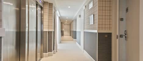 A modern hotel corridor with elevators, a carpeted floor, and a checkered wall pattern.