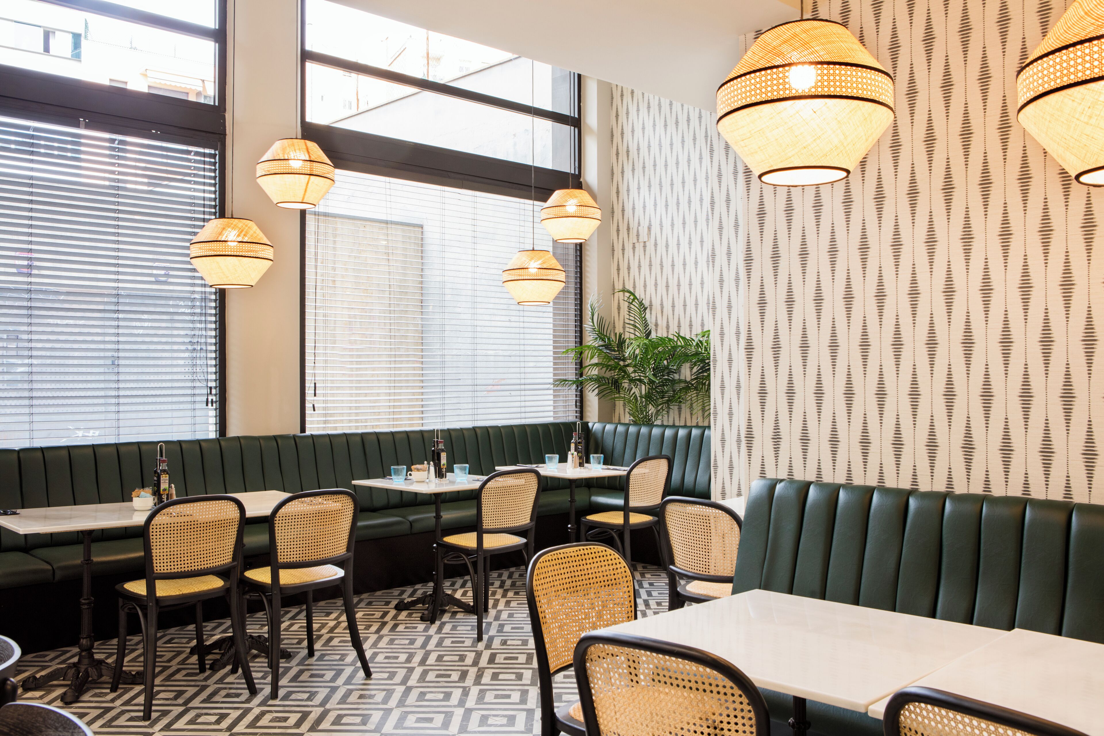 Een restaurantinterieur met groene banken, rieten stoelen en hanglampen.