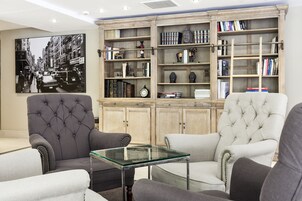 Una sala de estar con dos sillones tapizados, una mesa de centro de vidrio y una estantería llena de libros y objetos decorativos.