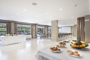 A spacious conference room with a long table set for a meeting, large windows, and a projector screen.
