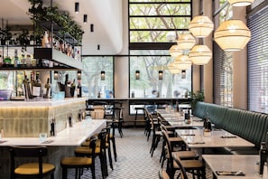 A restaurant interior with a bar area, seating, and large windows. - Hotel Acta City47 (Barcelona)