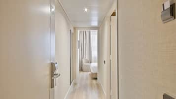 Un pasillo de hotel de diseño moderno, con suelo de tonos claros, techo con un diseño original y una cama con edredón blanco al fondo.