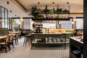 Un restaurante moderno con piso estampado, mesas de comedor con sillas, una zona de bar con estantes llenos de botellas y copas colgantes.