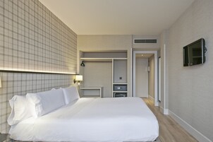A hotel room with a large bed, a wardrobe, a television, and a desk.