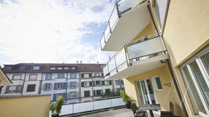 A balcony with a table and chairs, a potted plant, and a view of neighboring buildings. - BALEGRA City Hotel Basel Contactless Self Check-in (Basel)