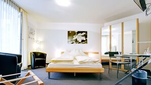 A hotel room with a bed, a desk, a chair, a lamp, and a large mirror. - BALEGRA City Hotel Basel Contactless Self Check-in (Basel)