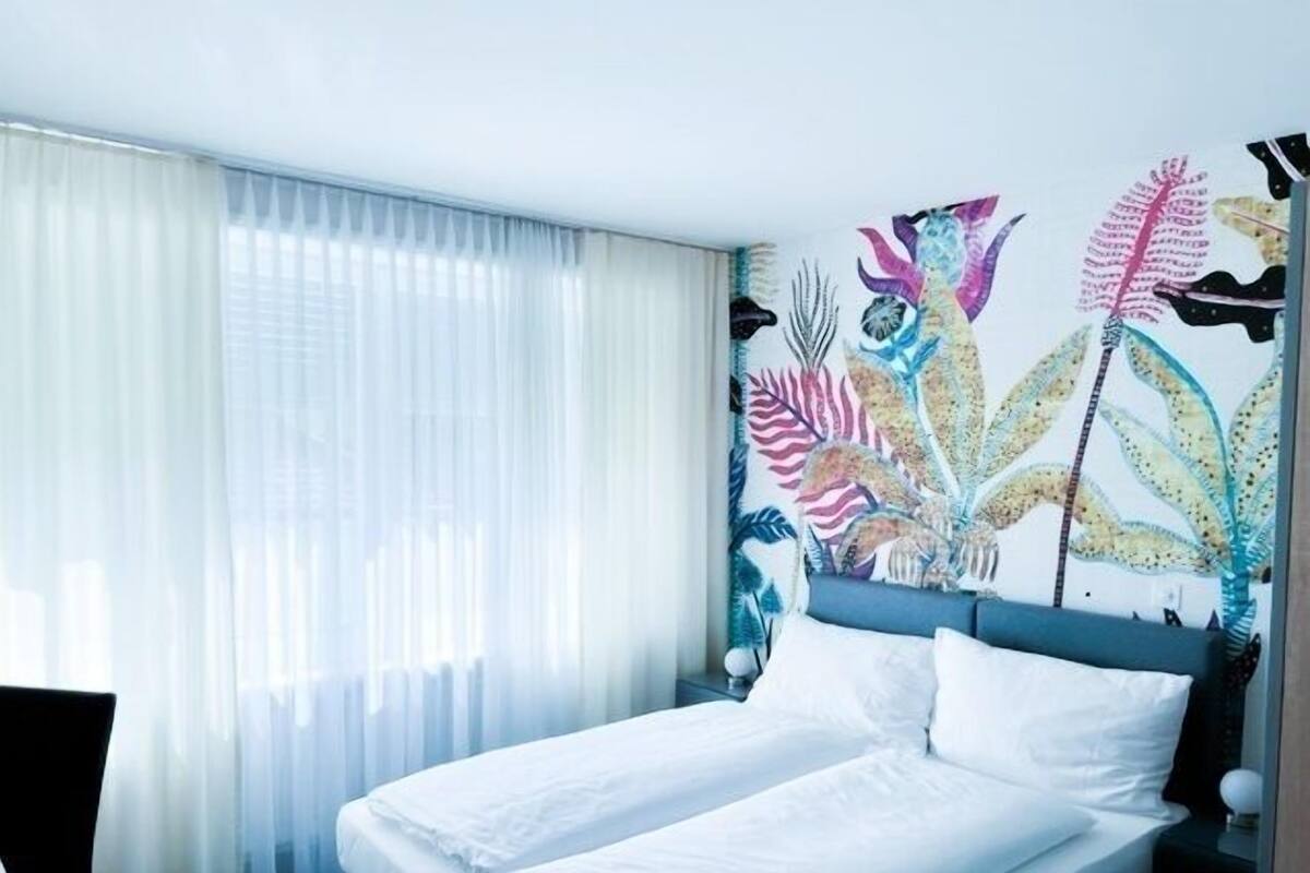 A hotel room with a bed, a nightstand, and a wall with a tropical leaf pattern.