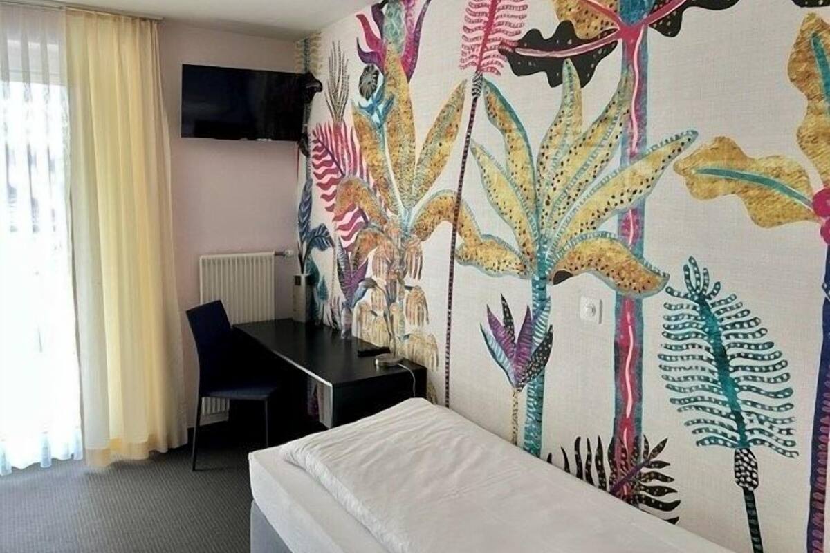 A hotel room with a bed, a desk, and a large floral tapestry on the wall.