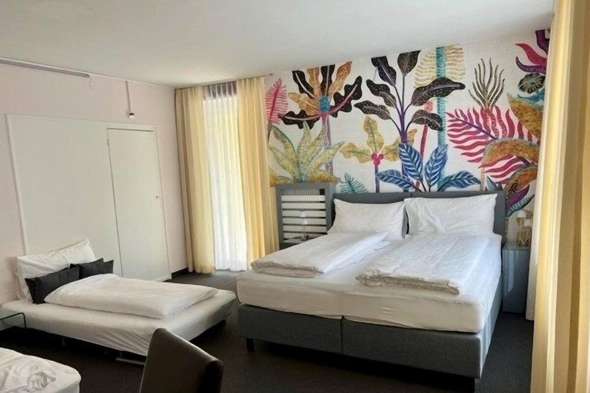 A hotel room with a bed, a chair, a wardrobe, and a wall with a floral mural.