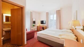 Una habitación de hotel con cama, escritorio, televisor y baño, además de una alfombra roja.