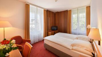 Una habitación de hotel con cama, dos sillas, televisión y escritorio con lámpara.
