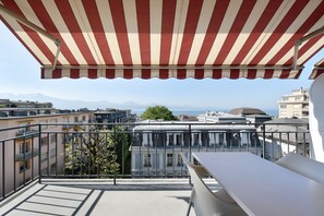Un balcón con un toldo a rayas, una mesa blanca y vistas a edificios y montañas.